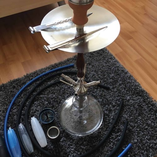 Shisha mit Glasbowl, Schlauch und Zubehör auf Teppich.