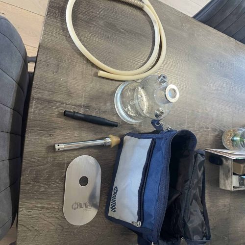 Wasserpfeife mit Zubehör auf Holztisch, Tasche im Bild.
