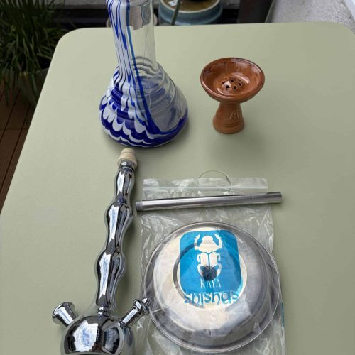 Bunte Glasbowl, Shisha-Adapter, Tabakdüse und Dichtungen auf Tisch.