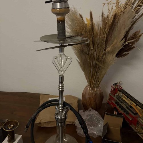 Shisha mit Glasbowl, Schlauch und Zubehör auf Tisch.