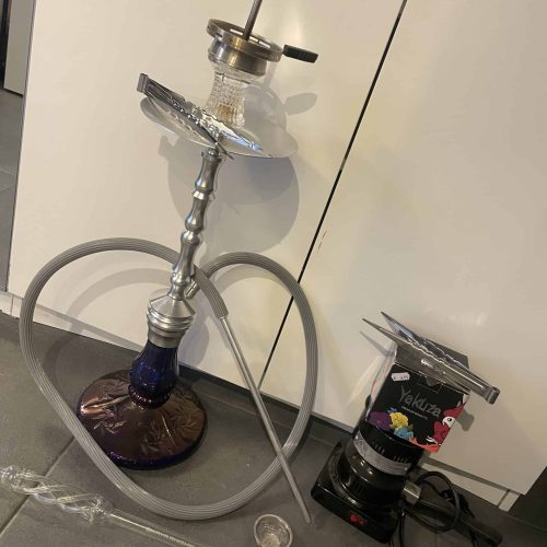 Shisha mit Glasbowl, Schlauch und Kohlezange auf Tisch.