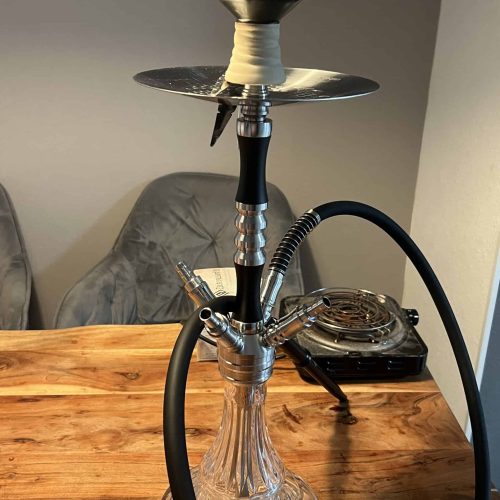 Rauchsäule mit Shisha-Kopf, Schlauch und Glasbasis auf Holztisch.