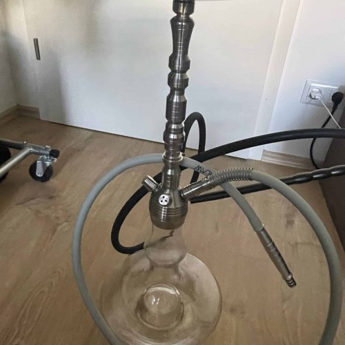 Shisha mit Glasbasis und Metallstamm, inklusive Schläuche, auf Holzboden.