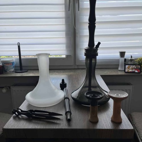 Verschiedene Shisha-Teile und Zubehör auf Tisch vor Fenster.