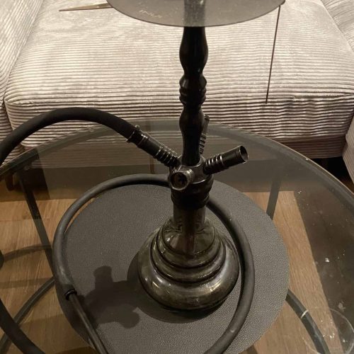 Rauch-Hookah mit Glasaufsatz, Schlauch und Zubehör, auf einem Tisch.