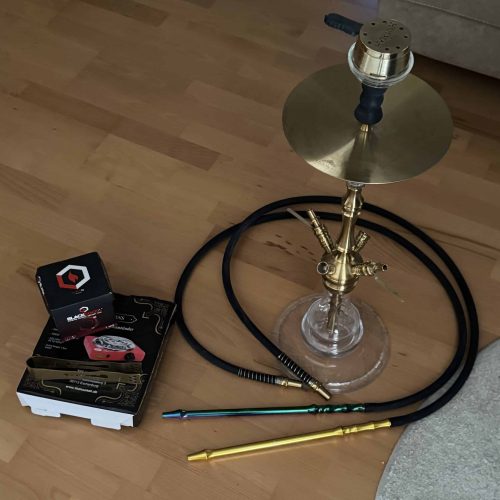 Shisha mit Glasbowl, Schlauch und Zubehör auf Holzboden.