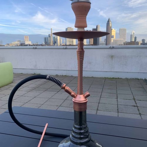 Schwarze Wasserpfeife mit Kupfer-Details auf einem Balkon mit Stadtblick.