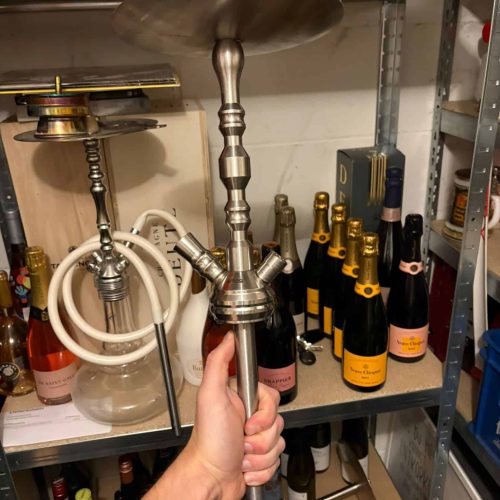 Hand hält eine Shisha mit Metallbasis in einem Lagerregal.