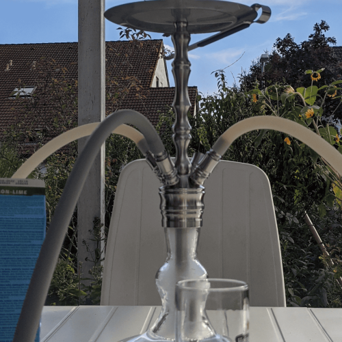 Shisha mit Wasserpfeife auf einem Tisch im Freien, Blick auf den Himmel und Bäume im Hintergrund.
