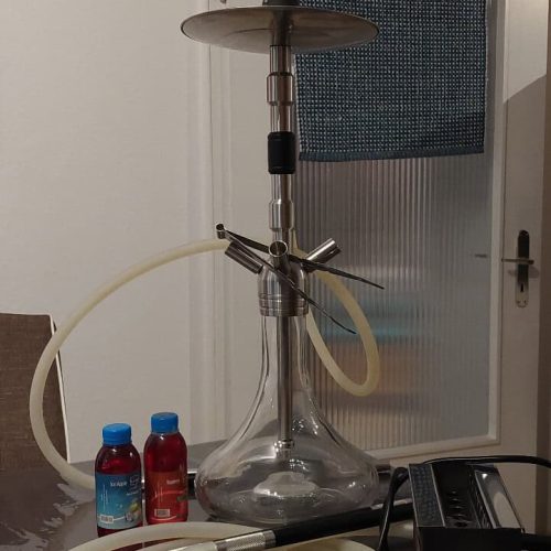 Shisha mit Rauchsäule, Schlauch und Zubehör auf Tisch.
