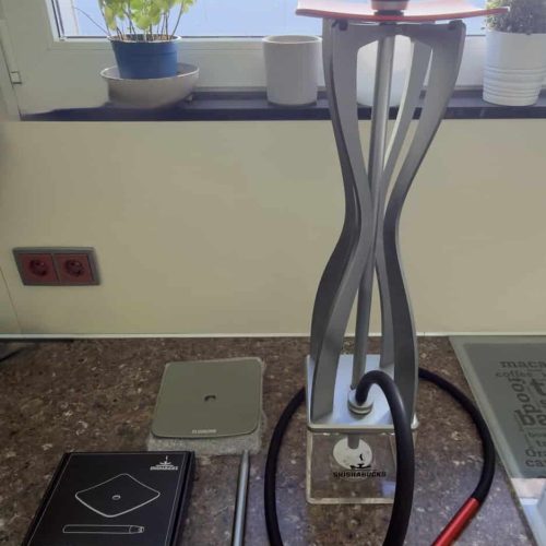 Shisha-Glasbowl mit Schlauch und Zubehör auf Tisch.