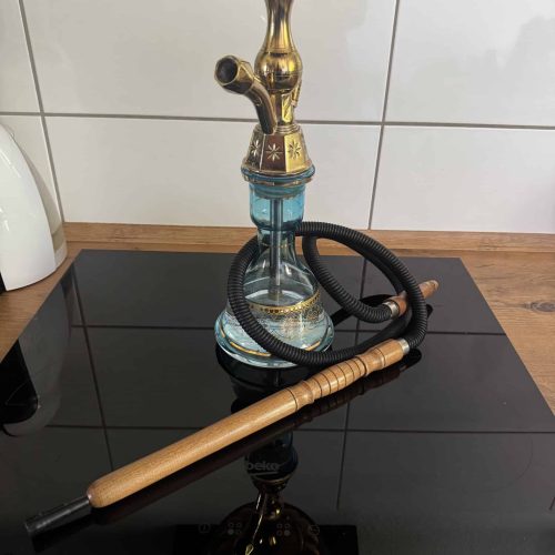 Shisha mit Glasbowl, Schlauch und Tonkopf auf schwarzer Oberfläche.