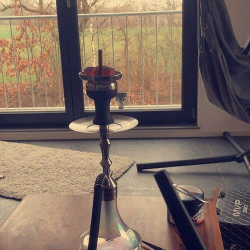 Shisha mit Wasserpfeife auf Tisch vor Fenster, Blick nach draußen mit Bäumen.