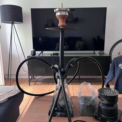 Shisha-Raucherset mit Kopf, Schlauch und Kohlehalter auf Tisch.
