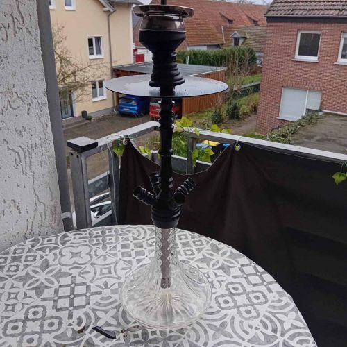 Rauchende Wasserpfeife auf Balkon mit Blick auf Nachbarhäuser.
