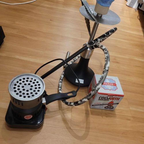 Shisha bowl with metal stem, hose, and coal tray auf Holzboden.