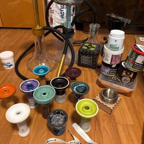 Verschiedene Shisha-Teile, Glasbowl, Tabakdosen und Zubehör auf Holztisch.