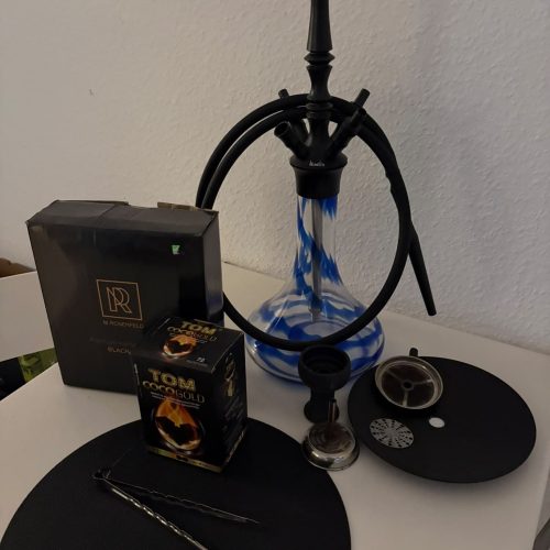 Shisha mit Glasbowl, Kohle, Zange und Zubehör auf Tisch.