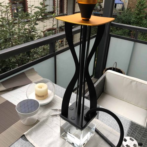Wasserpfeife mit schwarzem Schlauch und orangefarbenem Kopf, auf Balkon mit Stadtblick.