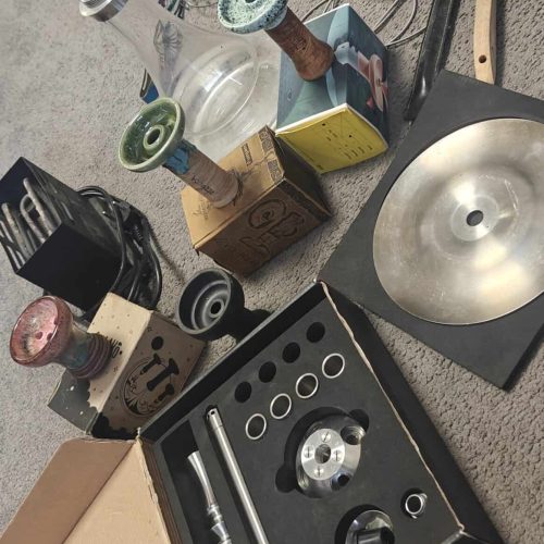 Verschiedene Shisha-Teile und Zubehör auf dem Boden verteilt.