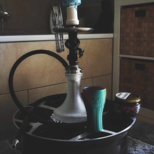 Shisha mit Glasbowl, Schlauch und Tabakbehälter auf schwarzem Tablett.