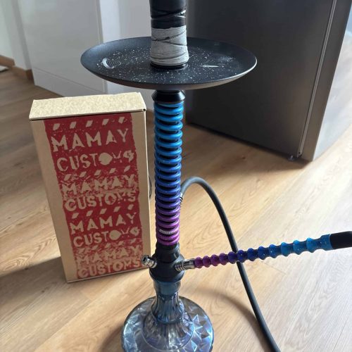Bunte Shisha mit farbiger Rauchsäule auf Holztisch.