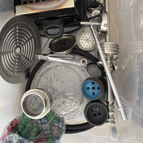 Verschiedene Shisha-Zubehörteile in einer Box, inklusive Glasbowl, Schlauch und Kohlezange.