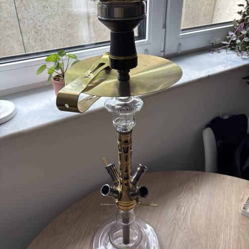 Shisha-Rauchsäule mit Glasbasis und Metallkopf auf Tisch.