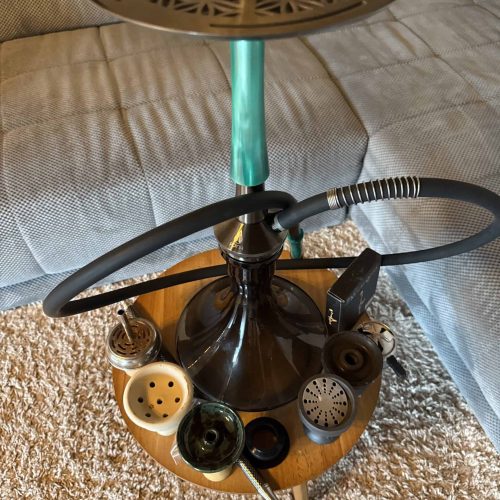 Shisha mit Glasbowl, Schlauch und Zubehör auf Holztisch.