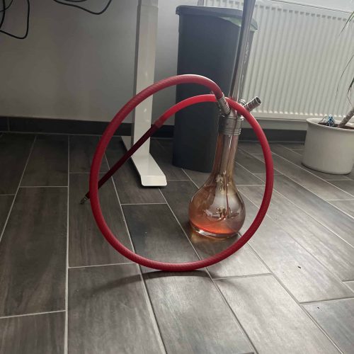 Shisha mit Glasballon und rotem Schlauch auf Fliesenboden.