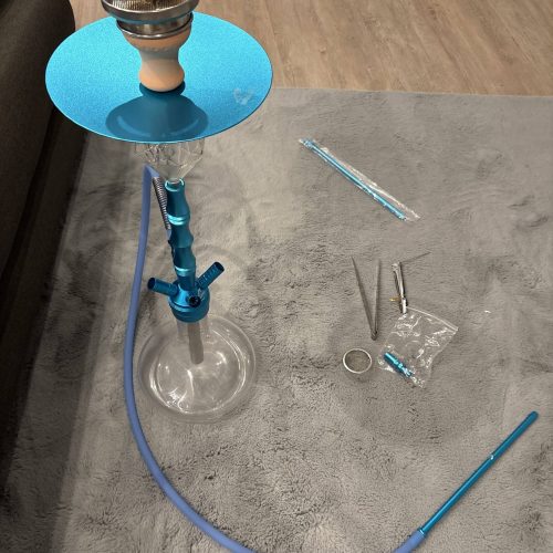 Shisha mit blauer Rauchsäule und Zubehör auf Teppich.
