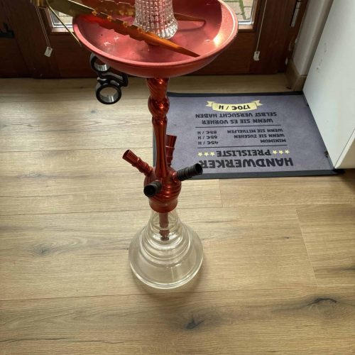 Rote Wasserpfeife mit Glasbasis und Zubehör, auf Holzboden.