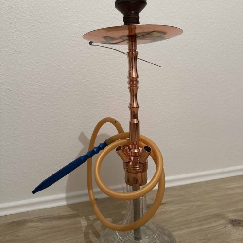 Shisha mit Glasbasis, Kupferrohr und Schlauch, auf Boden stehend.