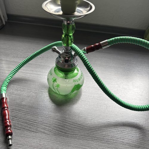 Wasserpfeife mit grüner Rauchsäule und Schlauch, auf Tisch.