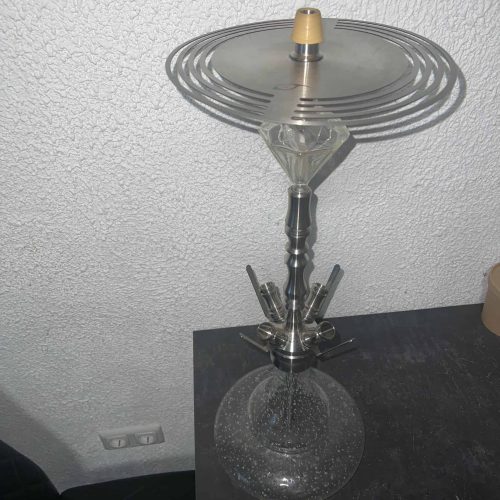 Glas-Shisha mit Metallaufsatz und runder Basis, auf Tisch.