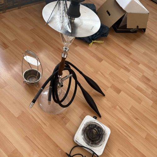 Shisha mit Glasbowl, Schlauch und Zubehör auf Holzboden.