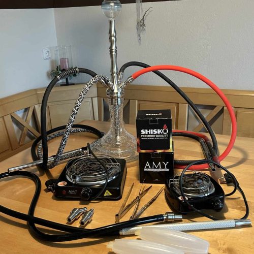 Shisha mit Glasbowl, Schlauch und Tabak auf Tisch.