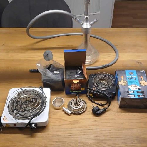 Verschiedene Shisha-Teile inklusive Glasbowl, Heizsystem und Zubehör auf Tisch.