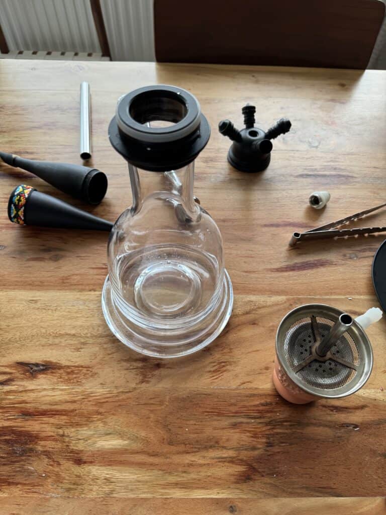 Glas-Shisha mit verschiedenen Zubehörteilen auf Holzoberfläche.