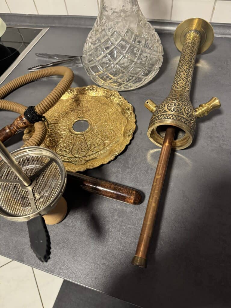 Verschiedene Shisha-Accessoires, darunter Glasbowl, Metallrohr und Dichtung.