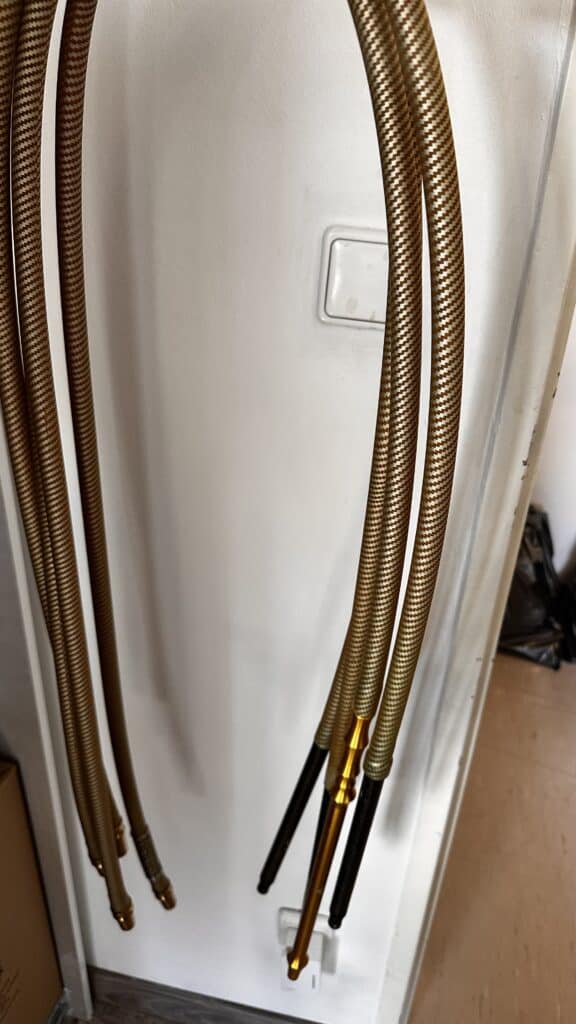 Mehrere goldene flexible Shisha-Schläuche hängen an einer weißen Wand.