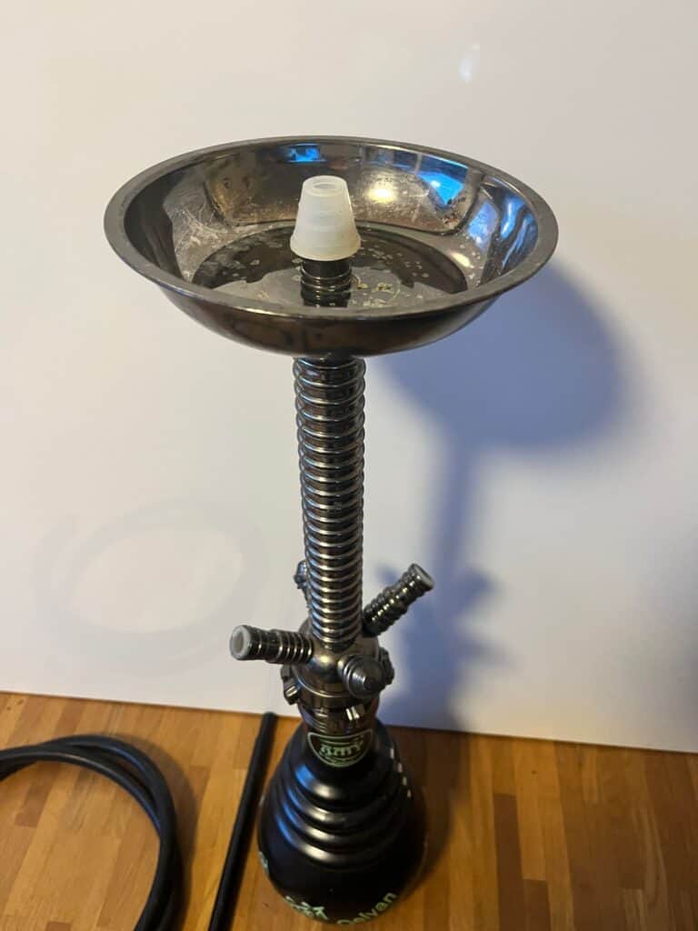 Shisha mit Wasserpfeife, Zubehör und Tabak für das Rauchen, auf einem Holztisch.