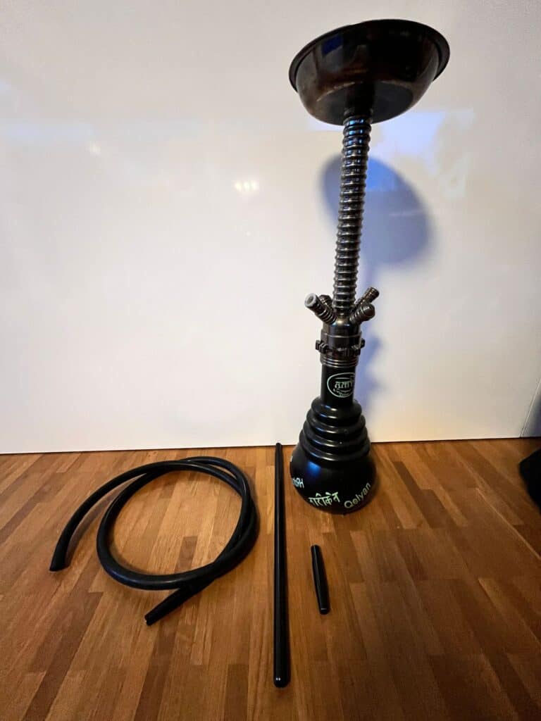Rauchvorrichtung für Shisha mit Schlauch, Zubehör und Basis, auf Holzboden.