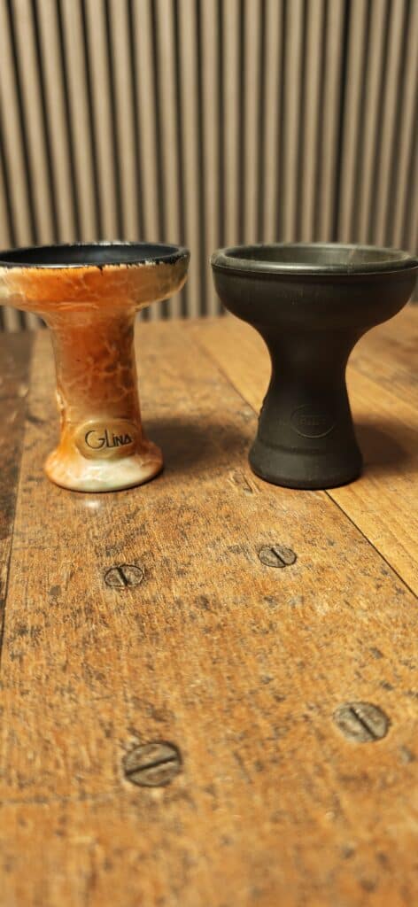 Zwei Shisha Glasbowl, eine orange, eine schwarze, auf Holzoberfläche.