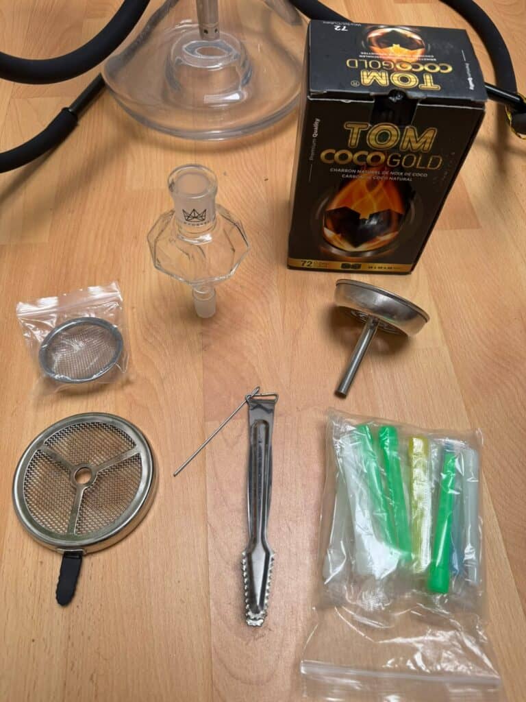 Verschiedene Shisha Zubehörteile, inklusive Glasbowl, Tauchrohr und Zange.