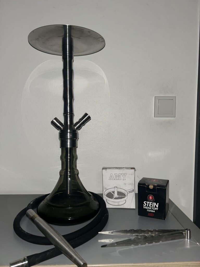 Rauch-Hookah mit Metallbasis, Tauchrohr und Zubehör, auf Tisch.