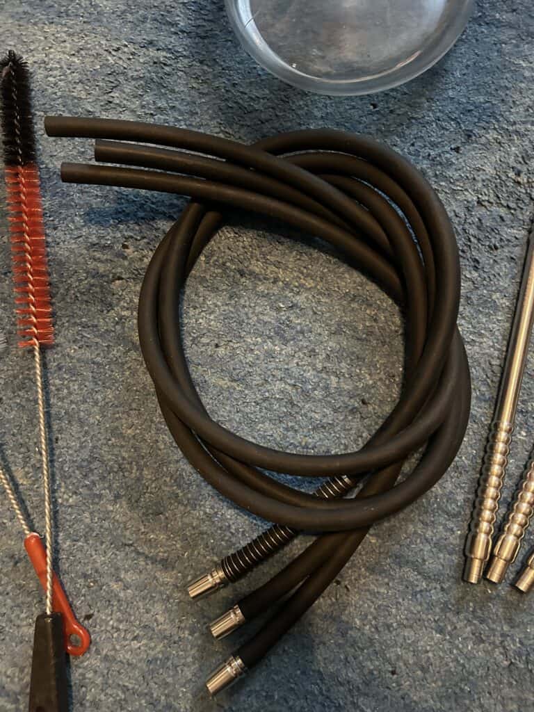 Schwarze Shisha Schläuche mit Metallanschlüssen auf Steinboden.
