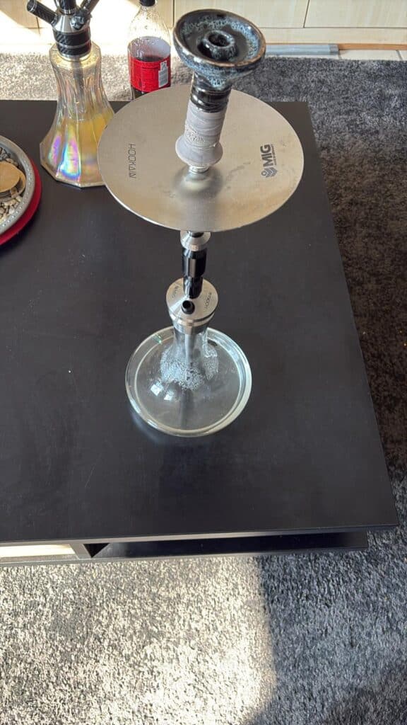Wasserpfeife mit Glasbasis, Metallrohr und Zubehör für Shisha-Rauchgenuss.