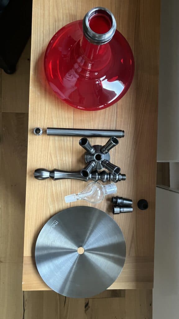 Rote Shisha Glasbowl mit Metall- und Glaszubehör auf Holz.
