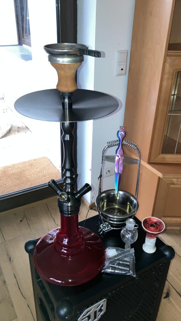 Shisha mit Glasbowl, Kopf und Zubehör auf Tisch.